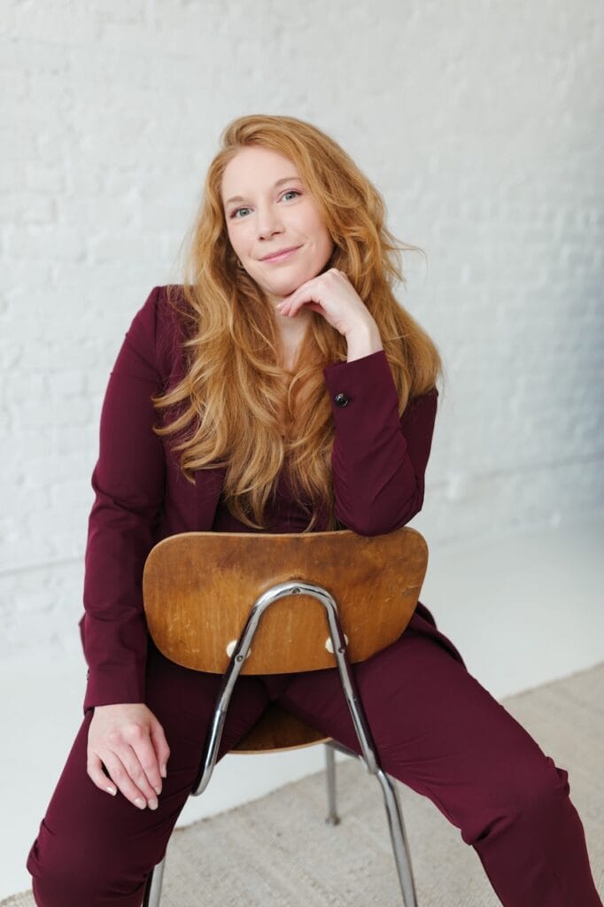 Cheryl Ann Barnes in a burgundy suit resting her chin on her hand, seated backward on a wooden chair