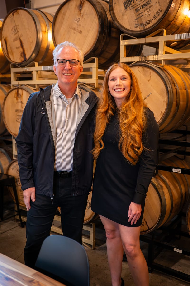 Cheryl Ann standing with a colleague in front of stacked whiskey barrels in Woodinville wine country